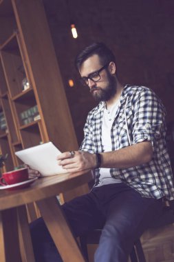 Yakışıklı genç hippi bir kafede dalgın dalgın oturuyor, sabah kahvesini içiyor, elinde bir tablet bilgisayar tutuyor ve internete yüklüyor.