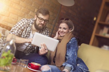 Genç çift bir kafede oturuyor, sabah kahvelerini içiyor, tablet bilgisayarda internette sörf yapıyor ve birlikte vakit geçiriyorlar.