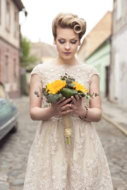 Güzelim gelin, elinde ayçiçeği buketi olan eski bir kaldırım kaldırımında gelinlik giymiş poz veriyor.