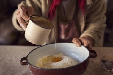 Yaşlı bir kadının ev yapımı makarna yaparken unun içine su döken elinin ayrıntıları. Seçici odak