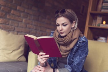 Güzel, modern bir kız bir koltukta oturup kitap okuyor.