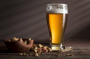 Çuval bezi altlığına konmuş soğuk soluk bir bira ve ahşap bir masada bir kase fıstık.