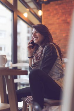 Çekici genç esmer bir kadın bir kafede oturuyor ve telefon görüşmesi yapıyor.