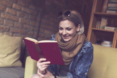 Güzel, modern bir kız bir koltukta oturup kitap okuyor.