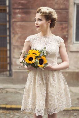 Güzelim gelin, elinde ayçiçeği buketi olan eski bir kaldırım kaldırımında gelinlik giymiş poz veriyor.