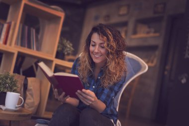 Güzel genç bir kadın bir kafede oturuyor, sabah kahvesinin tadını çıkarıyor ve kitap okuyor.
