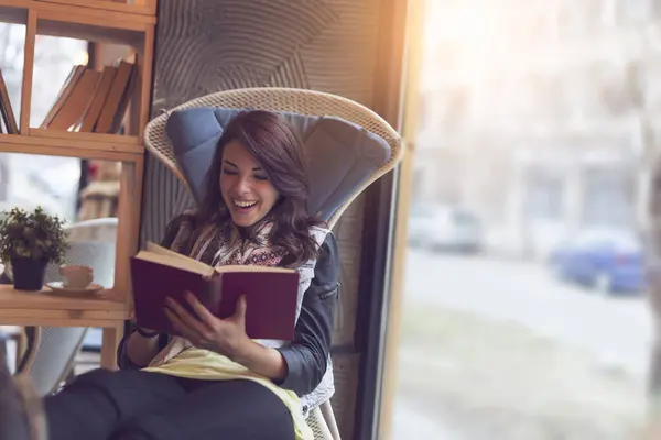 窓の隣のカフェに座っている美しい若い女性 笑顔で本を読んで — ストック写真