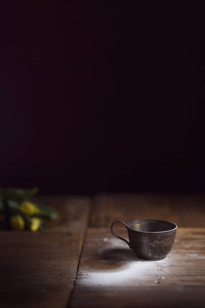Rustic metal cup placed on a wooden table sprinkled with flour. Selective focus