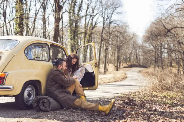 若いカップルは 道路に座って 彼らのルートを決定しようと 地図を見ている彼らのロード旅行で休憩を取るのが大好きです 女の子に焦点を当てる — ストック写真