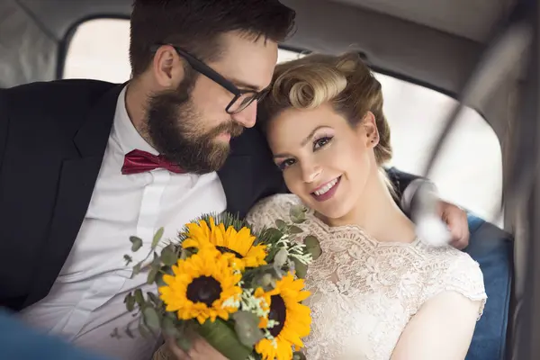 レトロなヴィンテージカーに座って ハグしてハネムーンで離れて行く若い新婚夫婦 — ストック写真