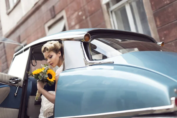漂亮的新娘穿着婚纱坐在旧车里 手持向日葵花束 — 图库照片