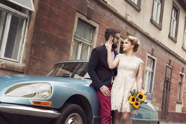 新婚夫妇站在鹅卵石街的一辆旧车旁边 拥抱并开始度蜜月 — 图库照片
