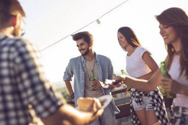 Bir grup genç arkadaş çatıdaki partide eğleniyor, barbekü yapıyor ve sıcak yaz günlerinin tadını çıkarıyorlar.