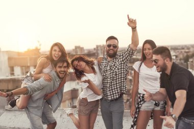 Bir grup genç yazın çatıdaki bir partide gün batımında eğleniyor. Ortadakilere odaklan.