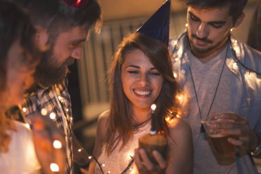 Bir grup genç arkadaş binanın çatısında doğum günü partisi veriyor, şarkı söylüyor ve mum üflüyorlar.