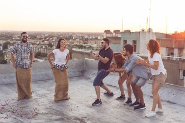 Bir grup genç yaz çatısı partisinde eğleniyor, yarışmacıları için tezahürat yapıyorlar.
