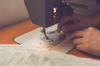 Genç tekstil işçisi dikiş makinesinin iğnesini çekiyor.
