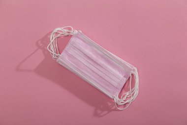 Pembe arkaplandaki pembe cerrahi maske yığınının üst görüntüsü. Bakteriyel ve viral enfeksiyonlara karşı koruma ekipmanının bir parçası olarak maskeler