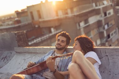 Birbirine aşık genç bir çift ananas kokteyli içiyor, gitar çalıyor ve gün batımında çatıdaki partide eğleniyor.