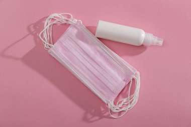Pembe tıbbi yüz koruma maskeleri ve Pembe arka planda izole edilmiş covid-19 salgınıyla mücadelede kullanılan alkol bazlı el dezenfektanı yığınının üst görüntüsü