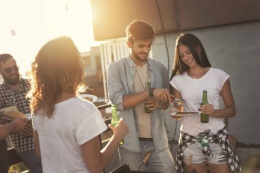 Bir grup genç arkadaş çatıdaki partide eğleniyor, barbekü yapıyor ve sıcak yaz günlerinin tadını çıkarıyorlar. Barbekünün yanındaki çifte odaklan.