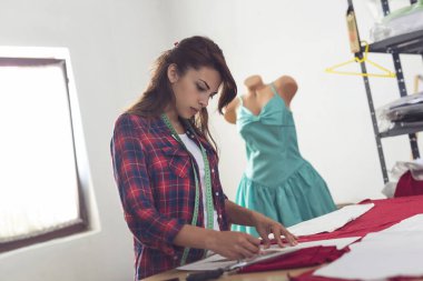 Terzi kadın tebeşirle bir kumaşa yeni bir elbise tasarımı çiziyor.