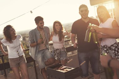 Genç arkadaşlar barbekü yapıyor, bira içiyor ve sıcak yaz günlerinin tadını çıkarıyor çatıdaki bir partide eğleniyorlar. Barbekünün yanındaki adama odaklan.