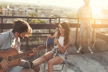 Genç arkadaşlar gitar çalıyor, şarkı söylüyor ve çatıdaki bir partide eğleniyorlar, sıcak yaz günlerinin tadını çıkarıyorlar..