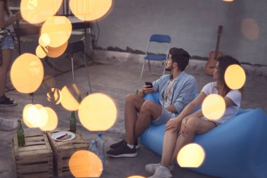 Bir grup genç, yaz tatili çatı partisinde eğleniyor. Kanepede oturan adama odaklan.