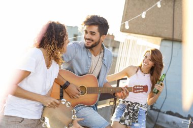 Üç genç arkadaş çatıdaki partide eğleniyor, gitar çalıyor ve şarkı söylüyorlar. Gitar çalan adama odaklan.