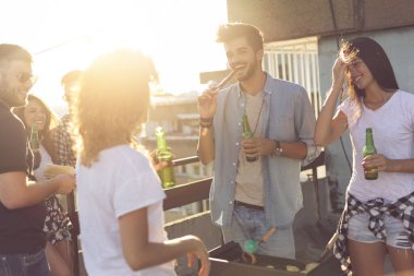 Bir grup genç arkadaş çatıdaki partide eğleniyor, barbekü yapıyor, bira içiyor ve sıcak yaz günlerinin tadını çıkarıyor. Yemek yiyen adama odaklan.