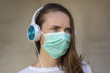 Tıbbi yüz koruma maskesi takan genç bir kadının portresi covid-19 önleme kampanyasının bir parçası olarak, müzik dinlerken ve salgın sırasında dinlenirken