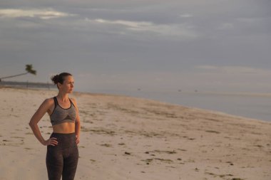 Genç bir kadın sabah antrenmanına ara veriyor, sahilde duruyor, güzel bir pistin yükselişini izliyor.