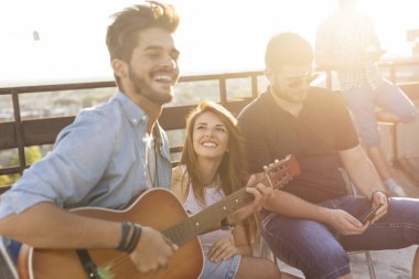 Bir grup genç arkadaş çatı partisinde eğleniyor, gitar çalıyor, şarkı söylüyor ve sıcak yaz günlerinin tadını çıkarıyor. Ortadaki kıza odaklan.