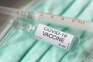 Bir tıbbi yüz koruma maskesinin üzerine yerleştirilen covid-19 aşı şişesi ve şırınganın yüksek açılı görüntüsü; yeni Coronavirus koruması, önleme ve tedavi araştırma konsepti