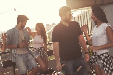 Genç arkadaşlar barbekü yapıyor ve sıcak yaz günlerinin tadını çıkarıyor çatıdaki bir partide eğleniyorlar. Barbekünün yanındaki adama odaklan.