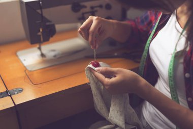 Genç terzi tamirat yapıyor, gömleğin düğmelerini elle dikiyor. Düğmeye odaklan.