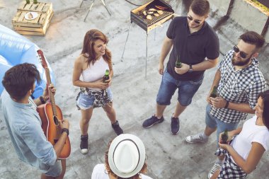 Çatıdaki bir partide eğlenen, gitar çalan, şarkı söyleyen ve sıcak yaz günlerinin tadını çıkaran bir grup genç arkadaşın en iyi görüntüsü. Sağdakilere odaklan.
