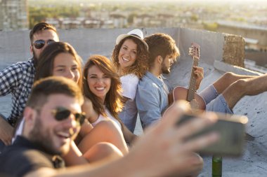 Bir grup genç gitar çalıyor, şarkı söylüyor ve çatıdaki bir partide eğleniyor.
