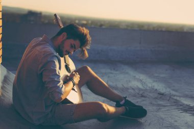 Adam binanın çatısında gitar çalıyor, dinleniyor ve sıcak yaz günlerinin tadını çıkarıyor.