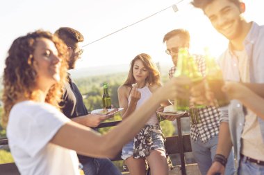 Bir grup genç arkadaş çatıdaki partide eğleniyor, bira içiyor, kadeh kaldırıyor ve sıcak yaz günlerinin tadını çıkarıyor. Çitin yanındaki çifte odaklan.