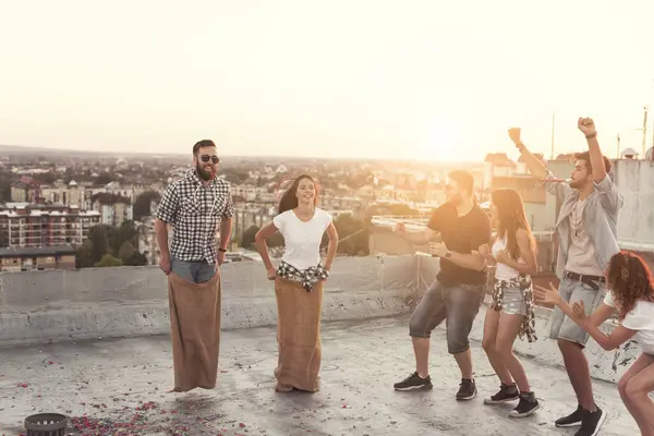 Bir grup genç yaz çatısı partisinde eğleniyor, yarışmacıları için tezahürat yapıyorlar.