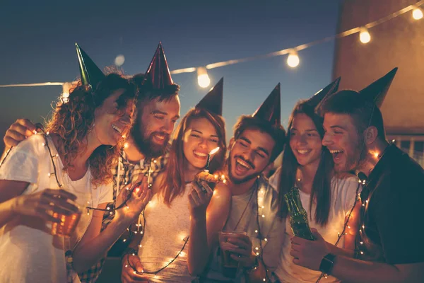 Group of young friends having a birthday party at a building rooftop, singing a song and blowing a candle. Focus on the candle and people on sides