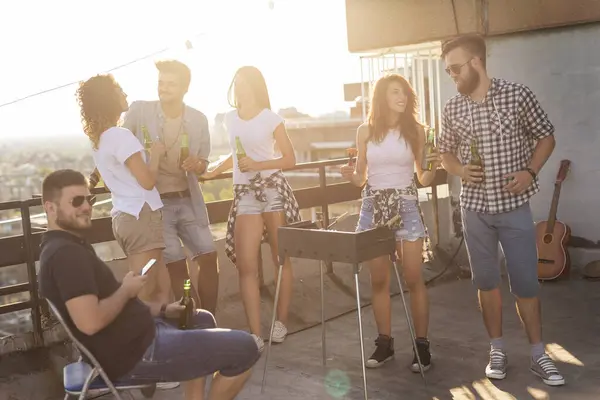 屋上パーティーで楽しんでいる若い友人のグループ バーベキュー ビールを飲み 暑い夏の日を楽しんでいます バーベキューの隣のカップルに集中する — ストック写真