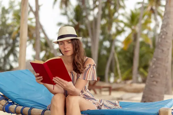 美しいトロピカルアイランドのエキゾチックなビーチリゾートでサンベッドの下に座っている若い女性は 海の上の日の出を楽しんで本を読んでリラックス — ストック写真