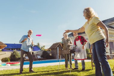 Bir grup neşeli, aktif son sınıf öğrencisi arka bahçede barbekü partisi veriyor, et ve sebze pişiriyor ve yakalamaca oynayarak eğleniyorlar.