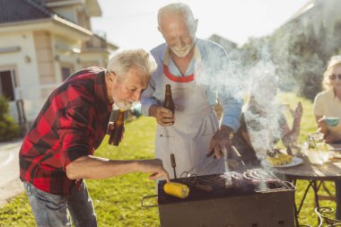 Yaşlı komşular bahçede et pişirirken eğleniyorlar, güneşli bahar günlerinde dışarıda dinleniyorlar.