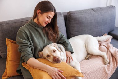 Bayan evcil hayvan sahibi, güzel Labrador köpeği kucağında uzanmış, ona sarılıp sarılıyor.