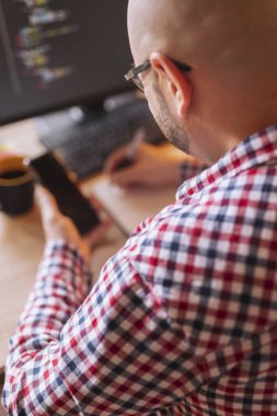 Akıllı telefon tutan ve evden uzaktan çalışırken not alan web geliştiricisinin yüksek açılı görünümü