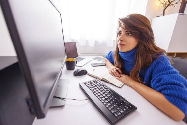 Kadın yazılım geliştirici, ofisteki masasında oturuyor, evden uzaktan çalışırken planlamacıdan notlar alıyor; kadın serbest çalışan ofis çalışanı